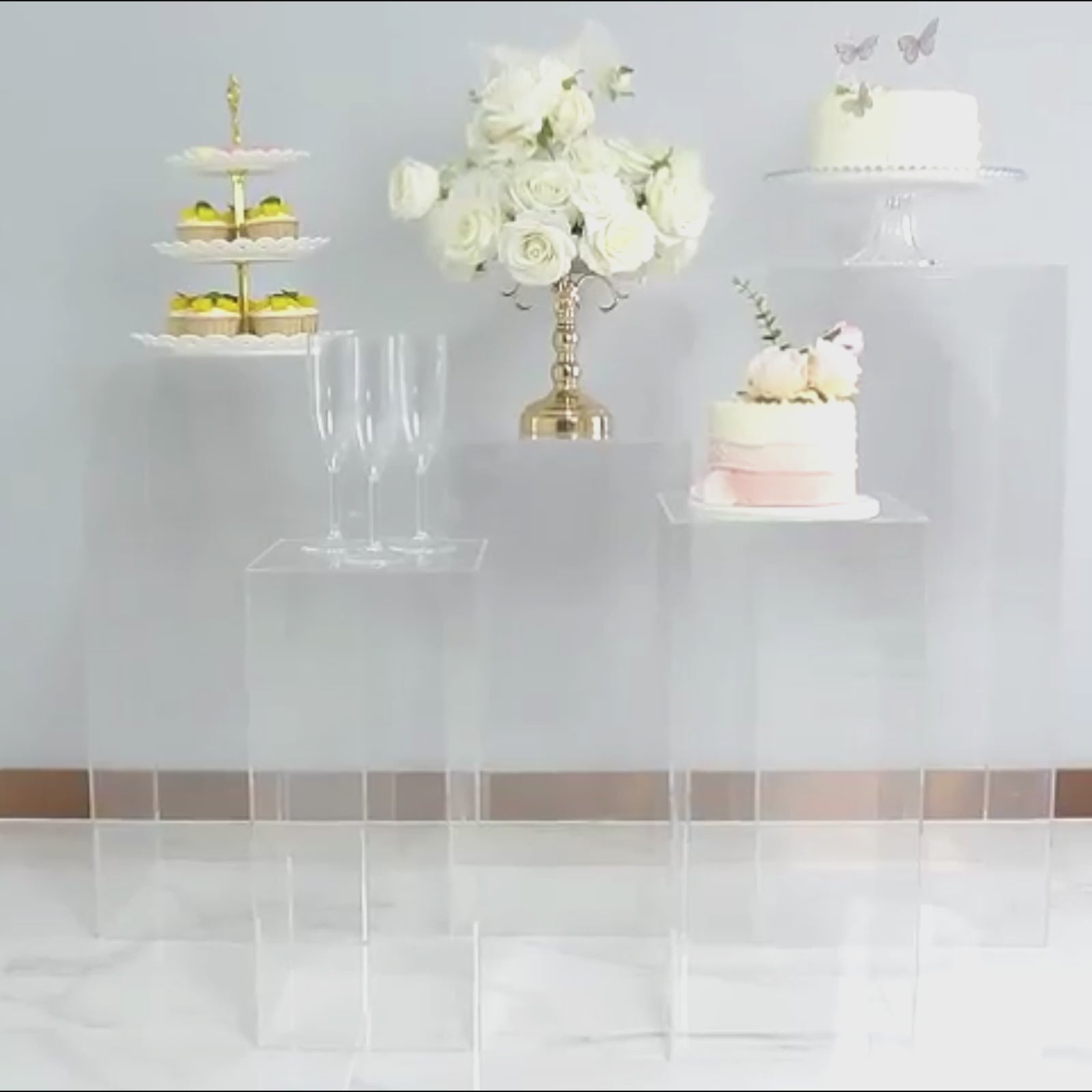 Clear acrylic pedestal stands displaying desserts and flowers.