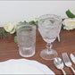 Clear vintage embossed goblets with floral design on a wooden table.