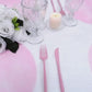 Pink disposable placemats on a dining table with glassware and flowers.