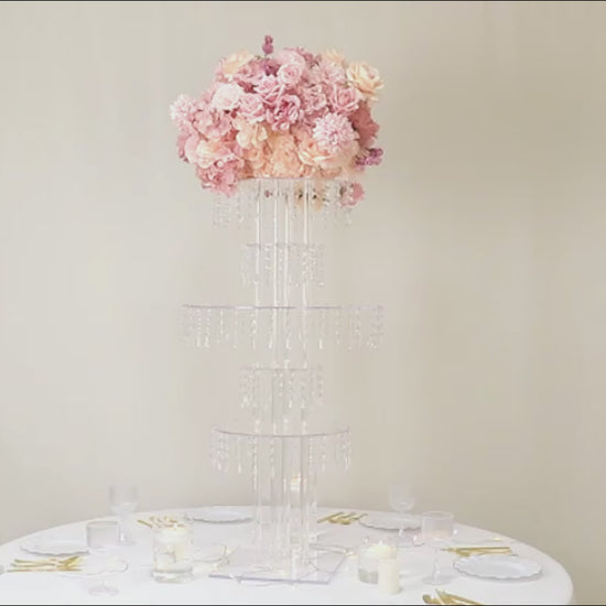 Clear acrylic chandelier flower stand with pink flowers and hanging crystals.