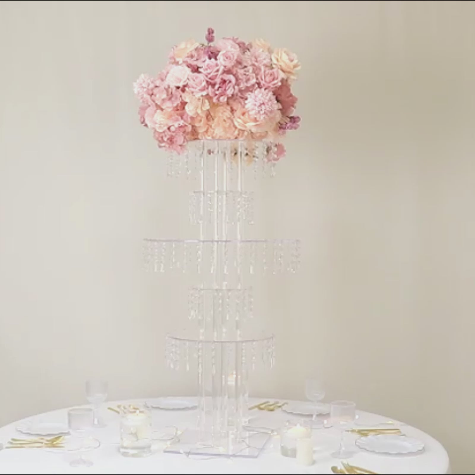 Clear acrylic chandelier flower stand with pink flowers and hanging crystals.