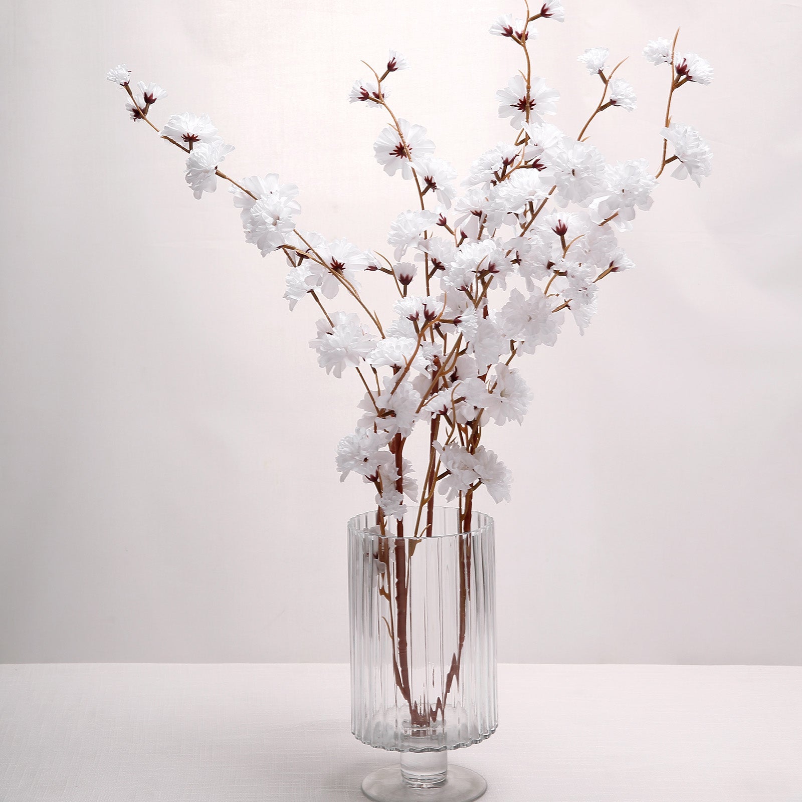 White artificial silk carnation flower stems in a clear glass vase.