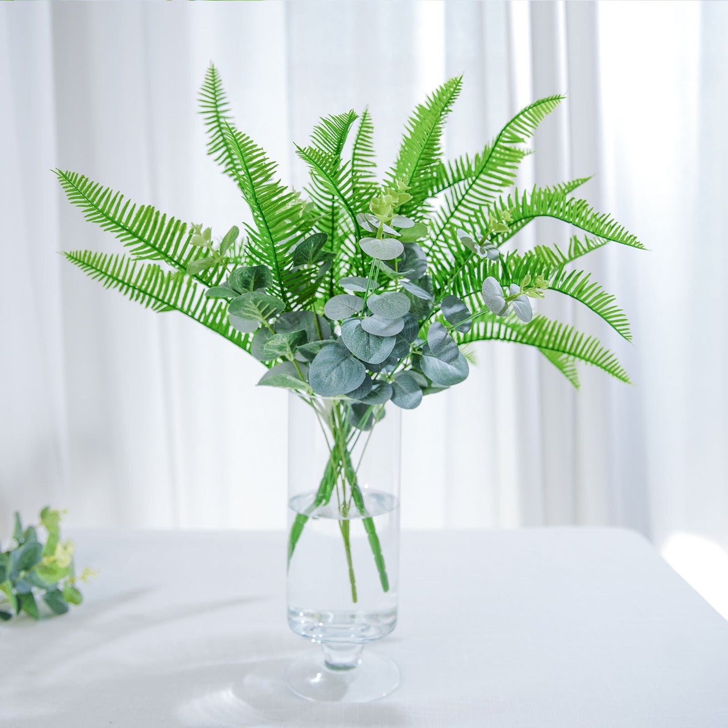 Artificial green cycas fern leaves in a clear vase.