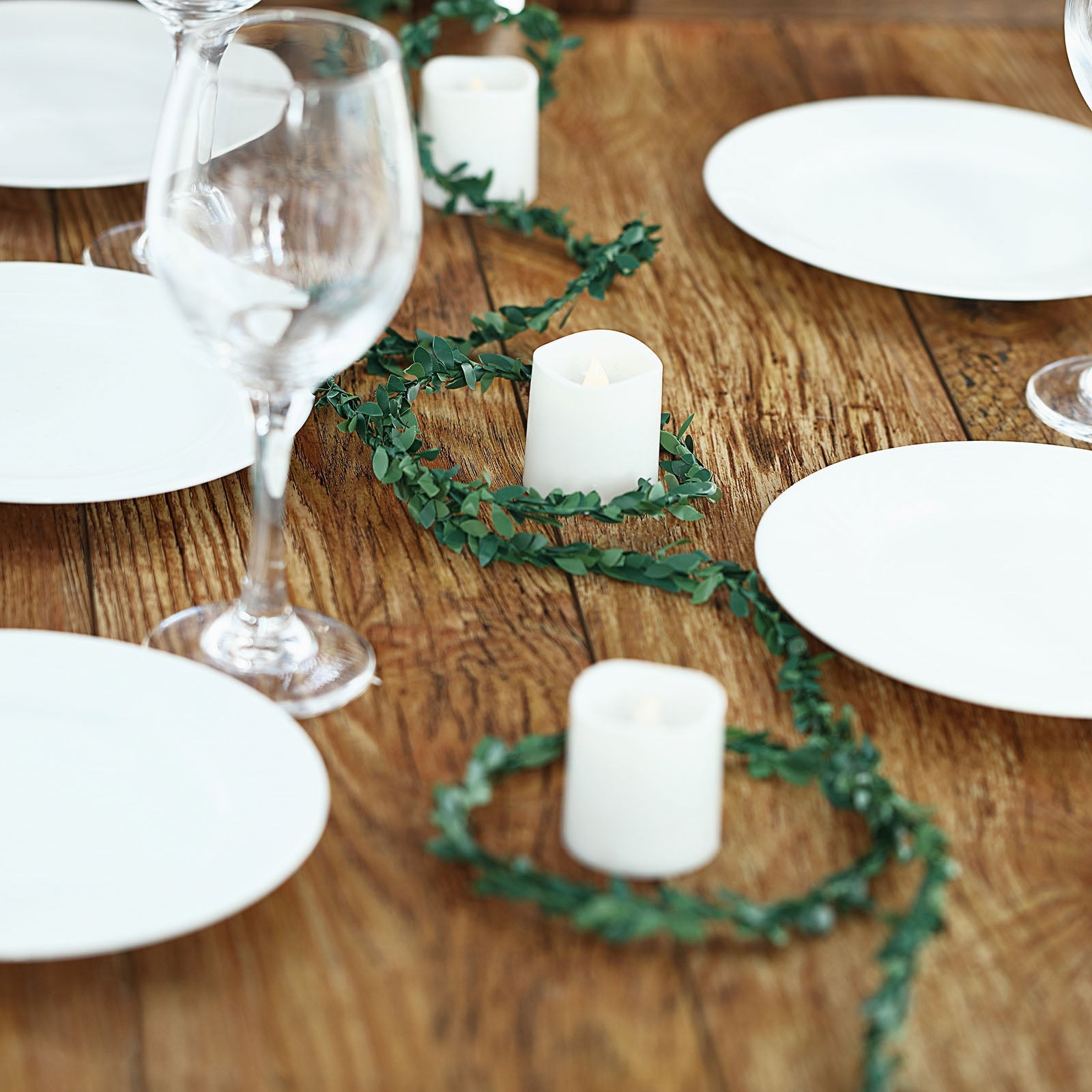 Mini green artificial leaf garland on a wooden table setting.