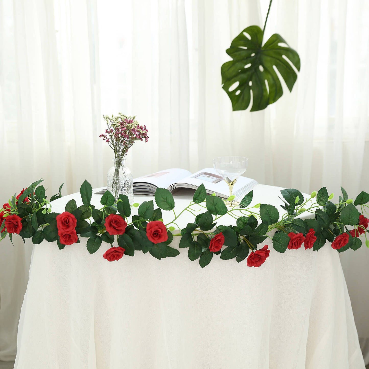 Red artificial silk rose flower garland hanging on a table.