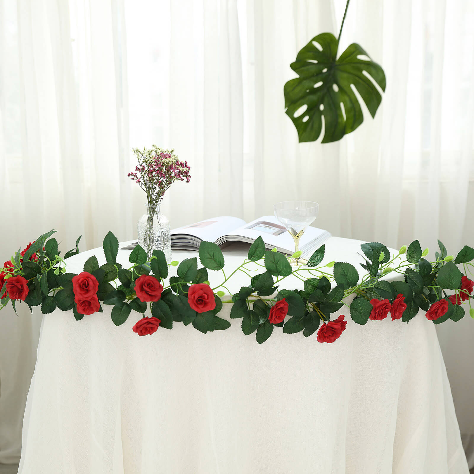 Red artificial silk rose flower garland hanging on a table.