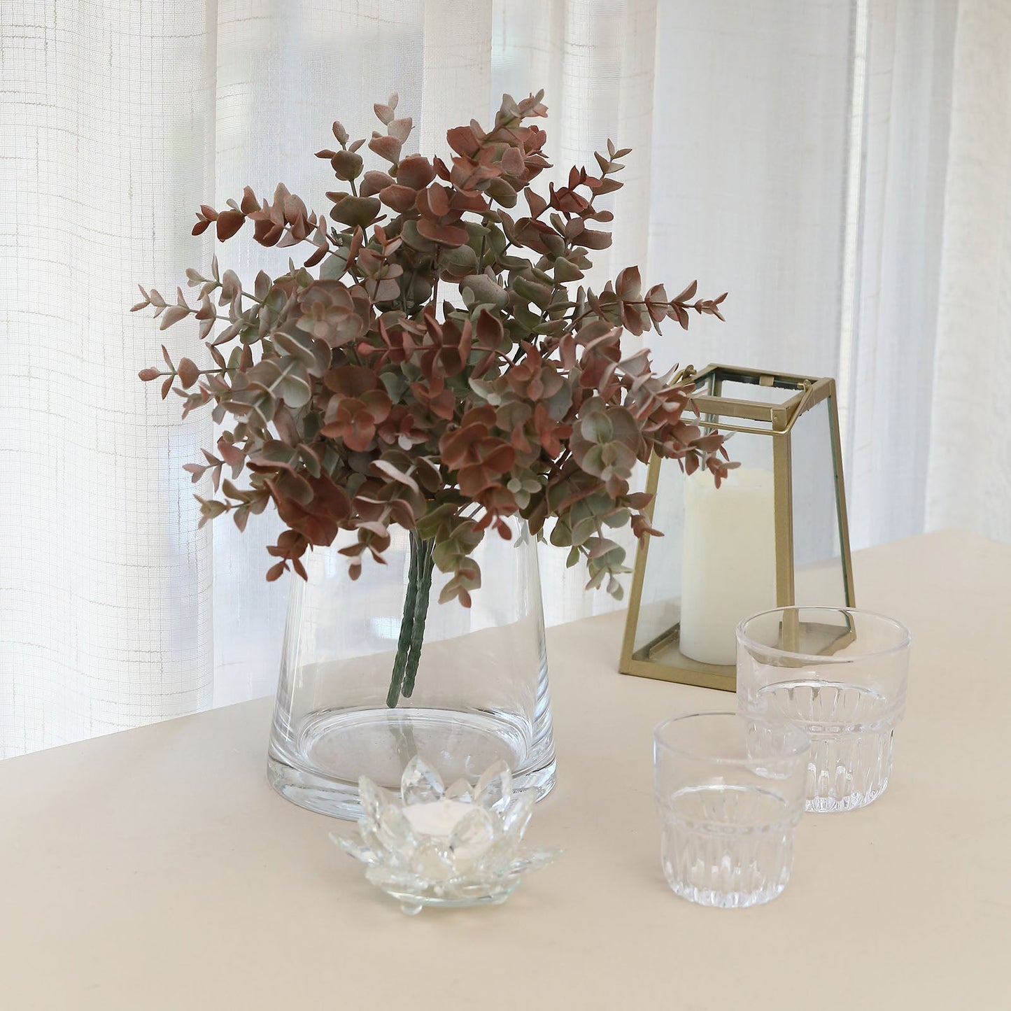 Frosted green and red artificial eucalyptus plant in a clear vase.