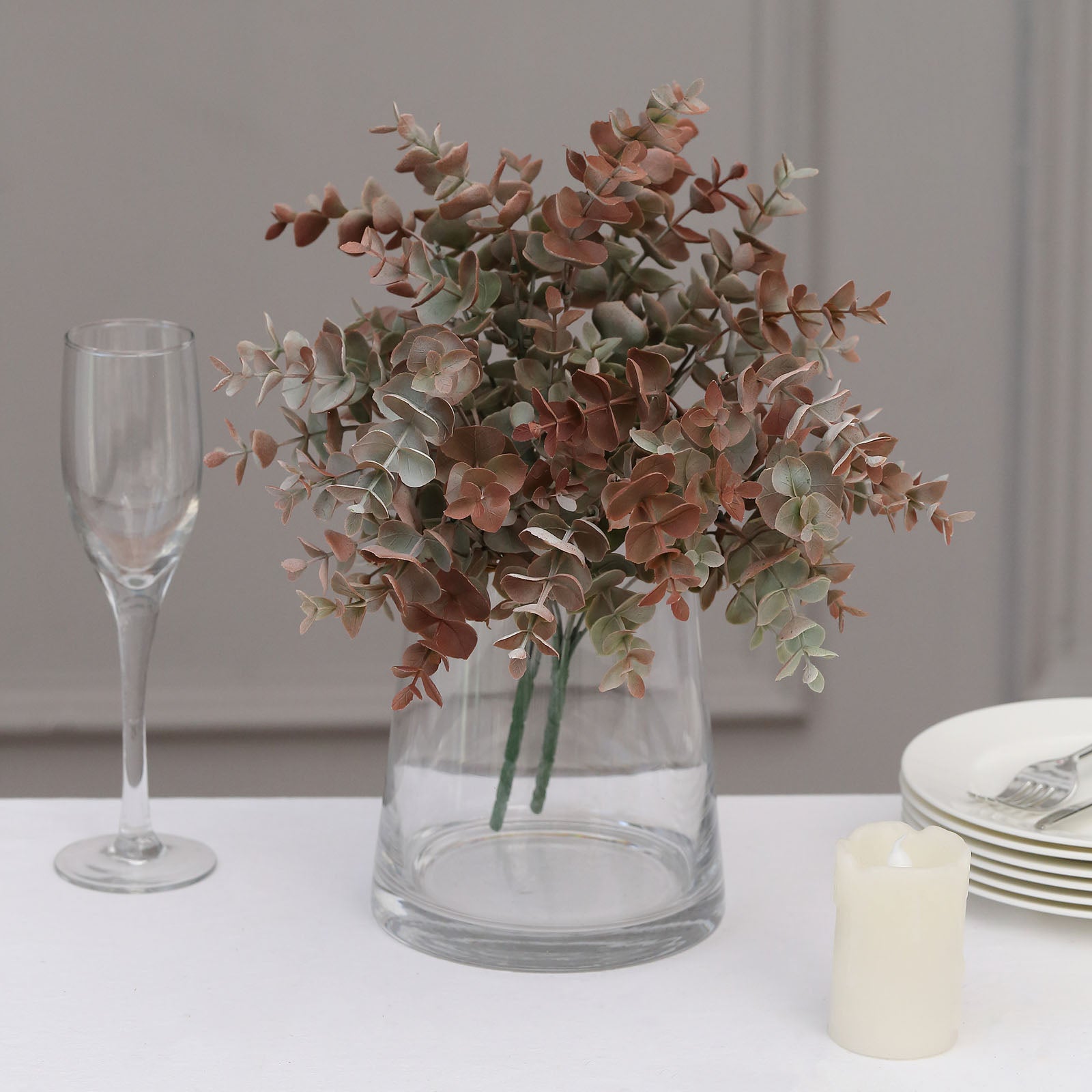 Frosted green and red artificial eucalyptus plants in a clear vase.