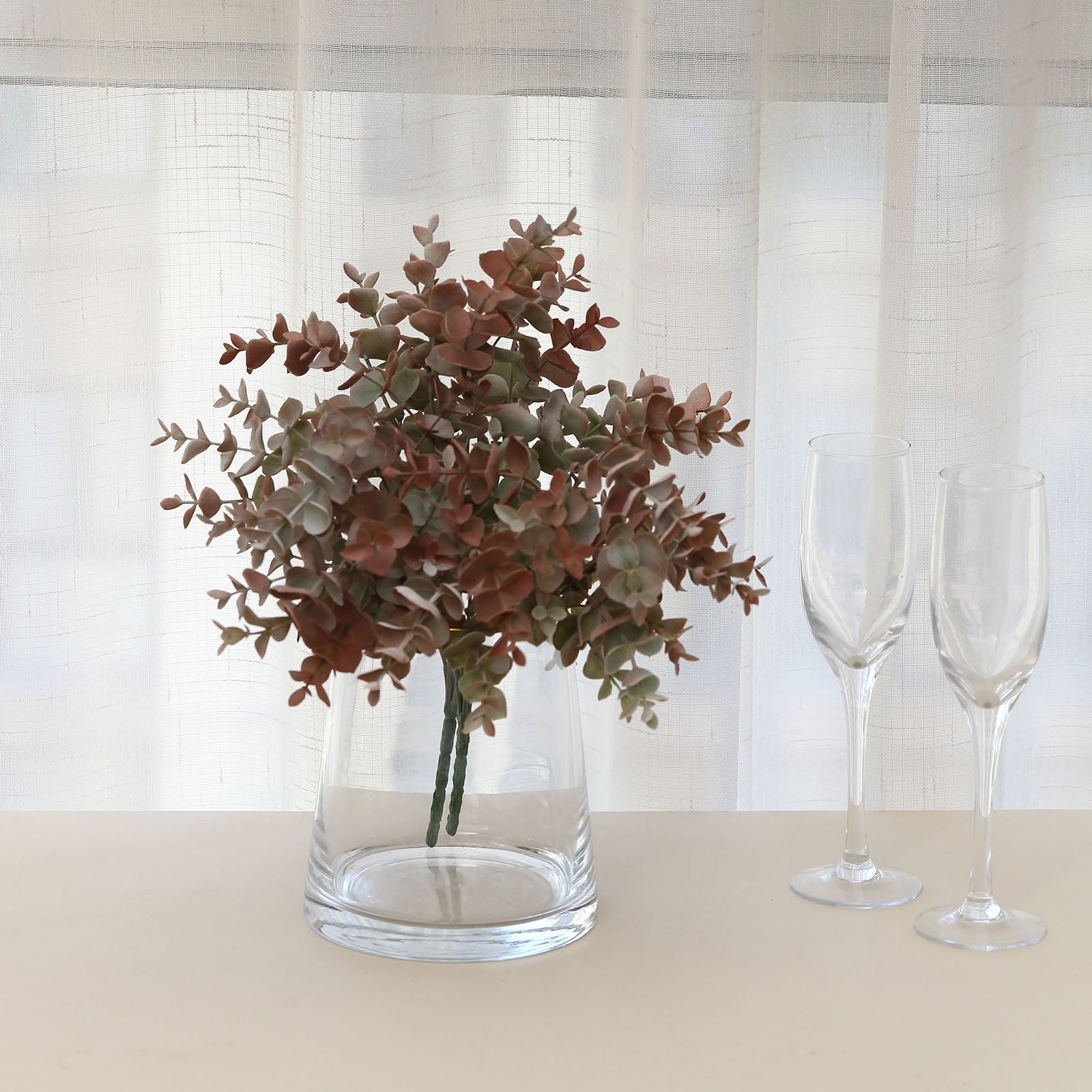 Frosted red artificial eucalyptus plant in a glass vase.
