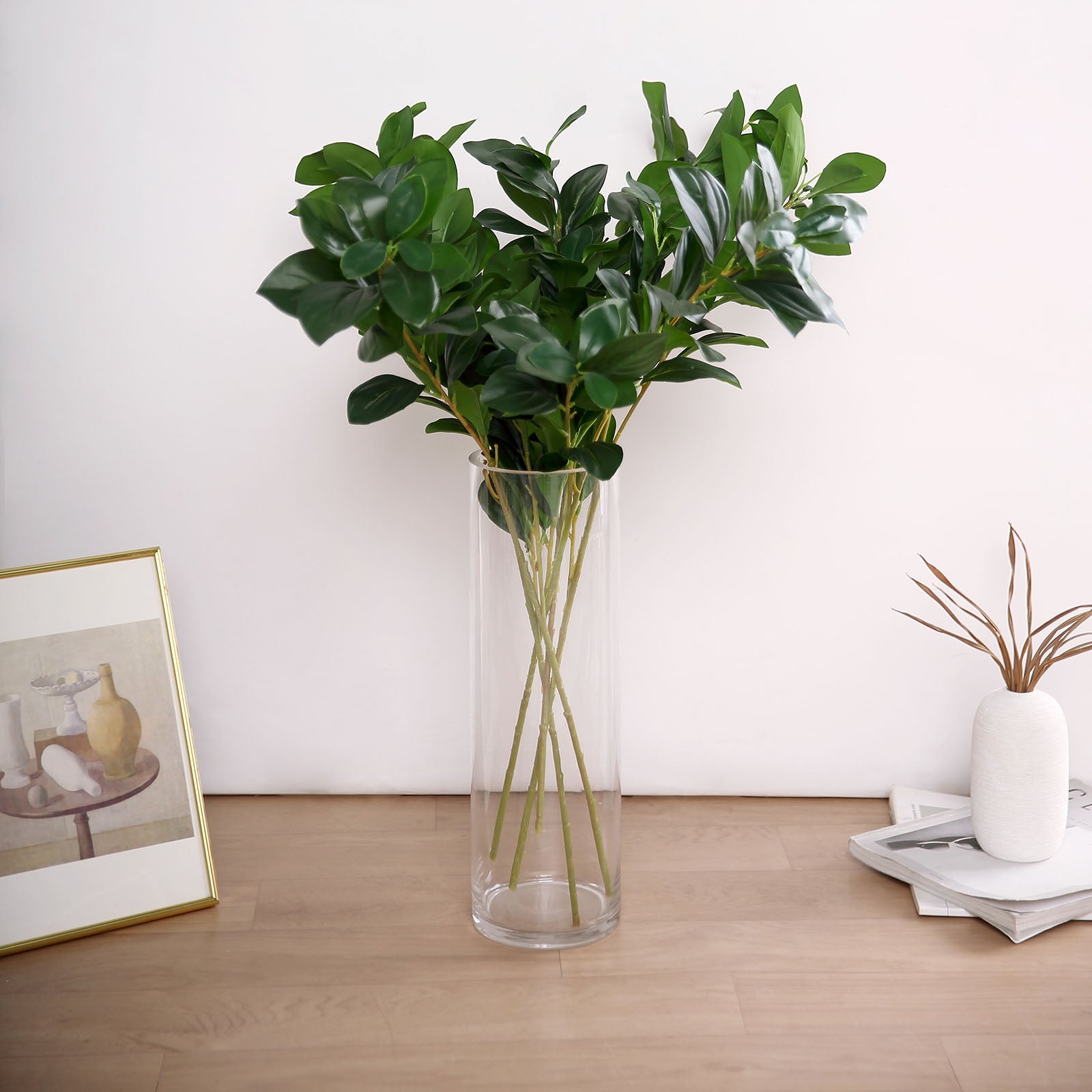 Green artificial lemon leaf branches in a clear vase.