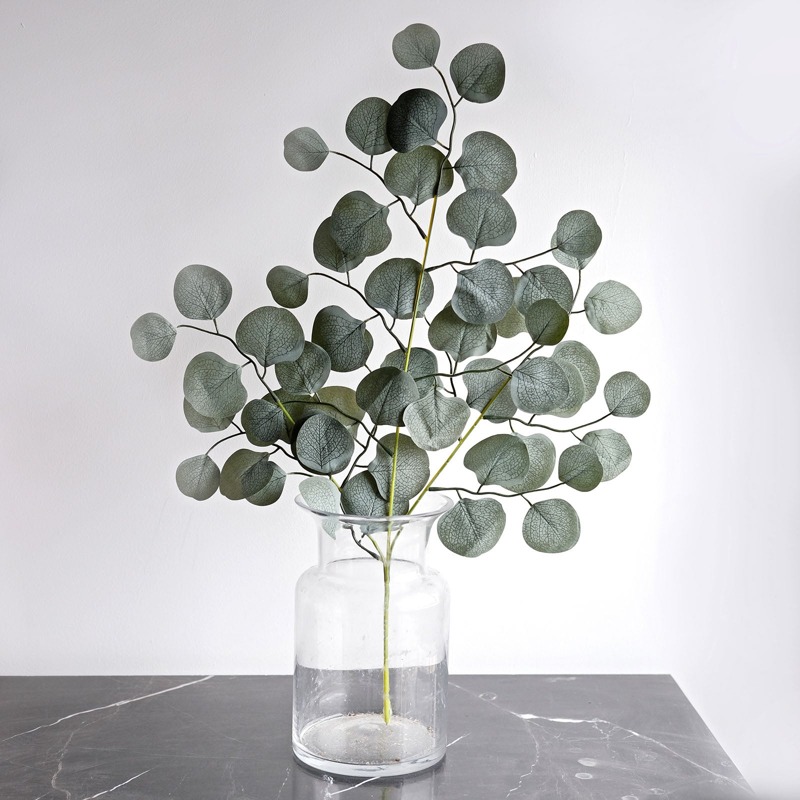 Frosted green artificial silk eucalyptus leaf stems in a glass vase.