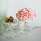 Blush artificial satin hydrangeas in a clear vase on a table.