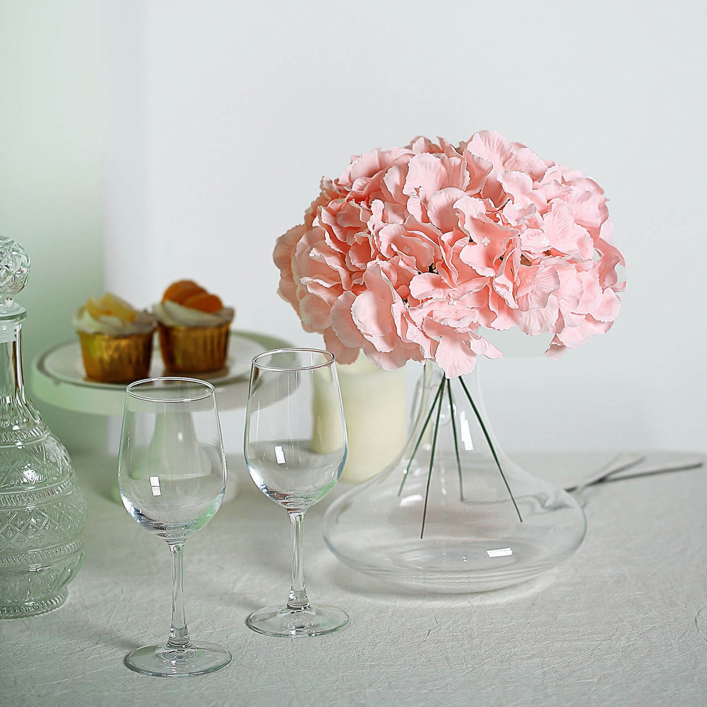 Blush artificial satin hydrangeas in a clear vase on a table.