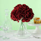 Burgundy artificial satin hydrangeas in a clear vase on a table setting.