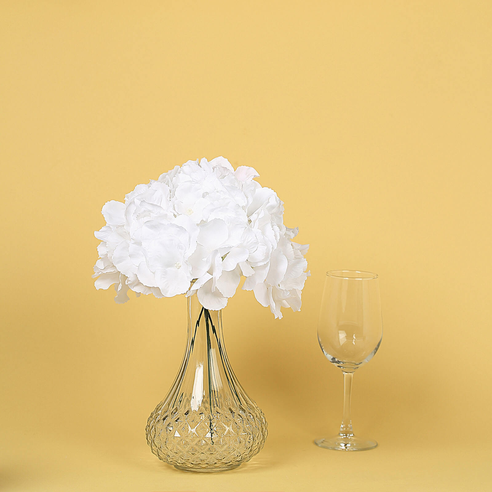 White artificial satin hydrangeas in a clear glass vase.