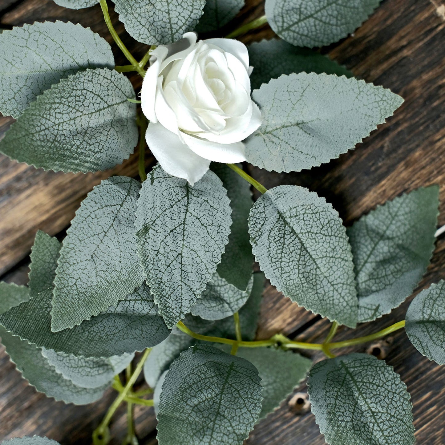 Frosted green artificial rose leaves with a white flower for DIY projects.