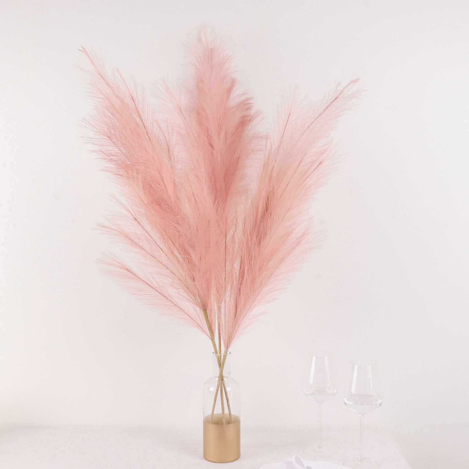Dusty rose artificial pampas grass in a vase with two glasses.