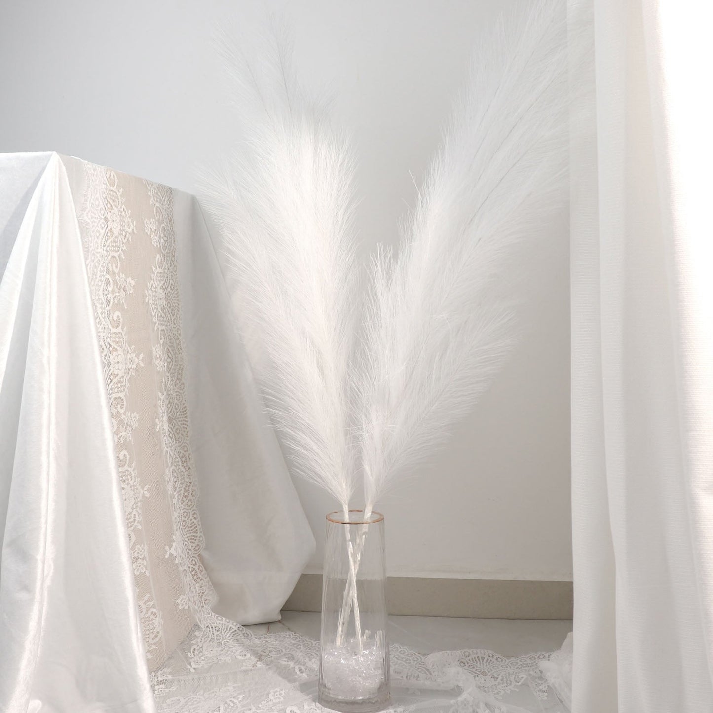 White artificial pampas grass plant sprays in a glass vase.