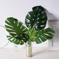 Assorted green artificial silk tropical monstera leaf plants in a vase.