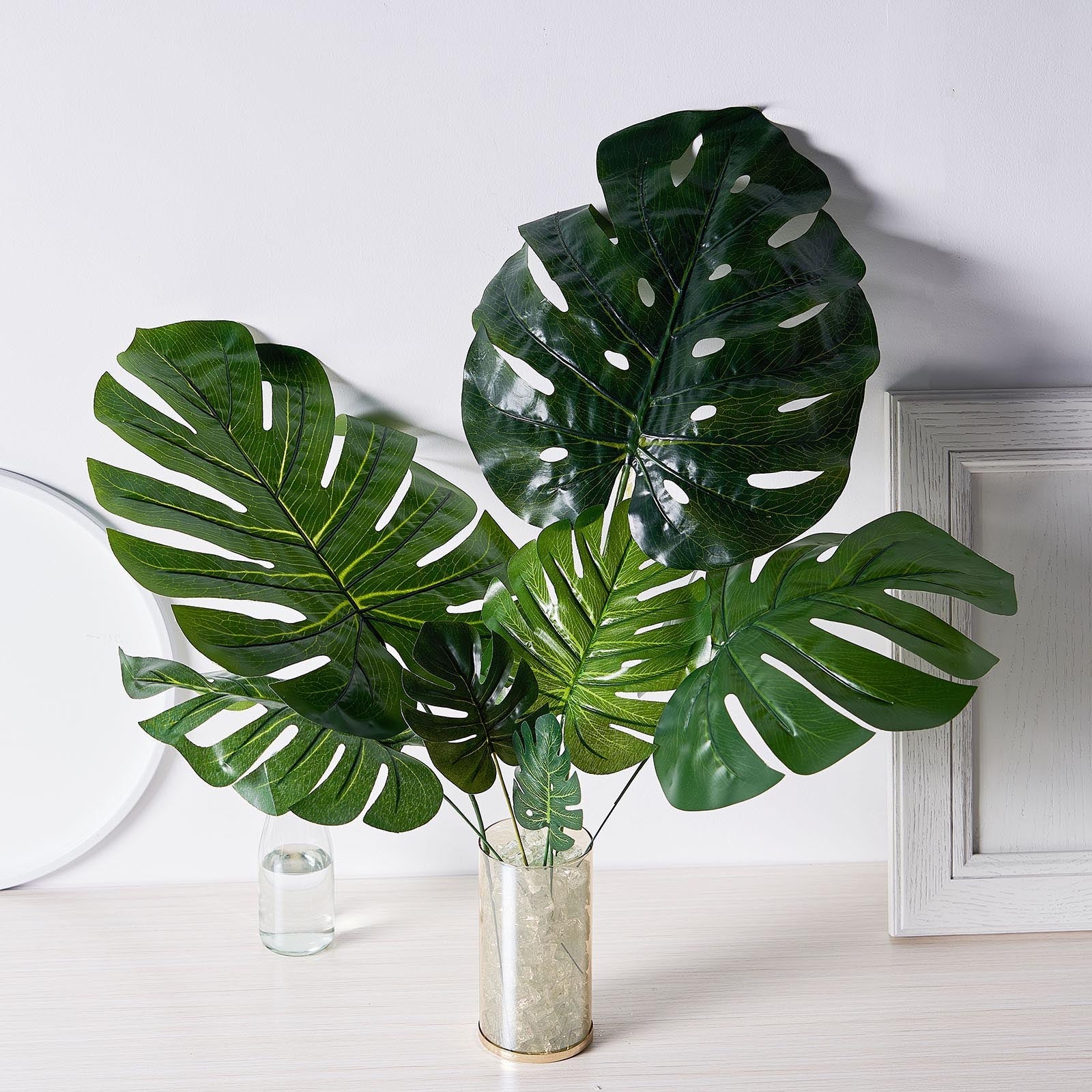 Assorted green artificial silk tropical monstera leaf plants in a vase.