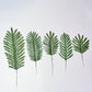 Assorted green artificial silk tropical palm leaves on a white background.