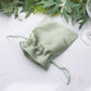 Sage green satin drawstring wedding favor gift bag on a white surface.