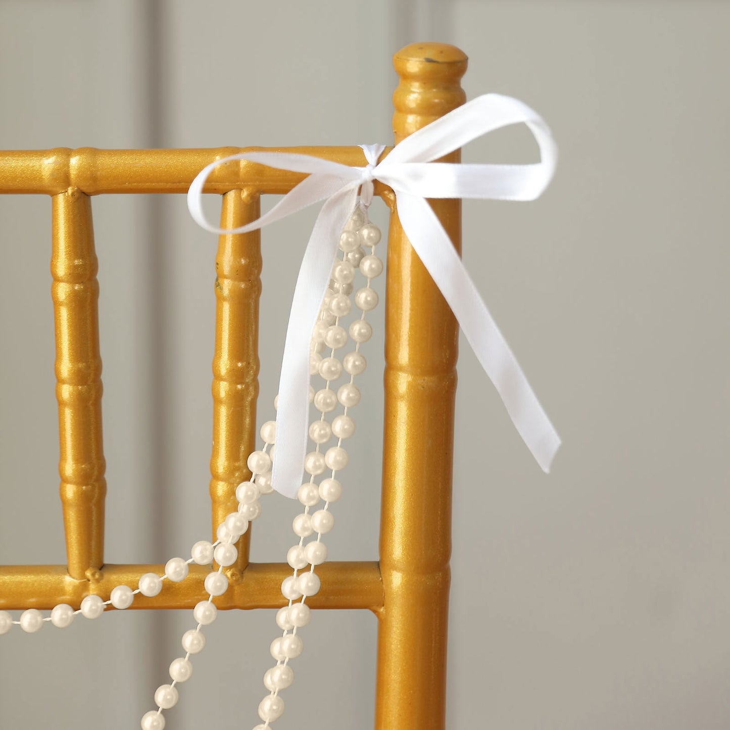 Ivory faux pearl beaded chair back garland with bow on a gold chiavari chair.