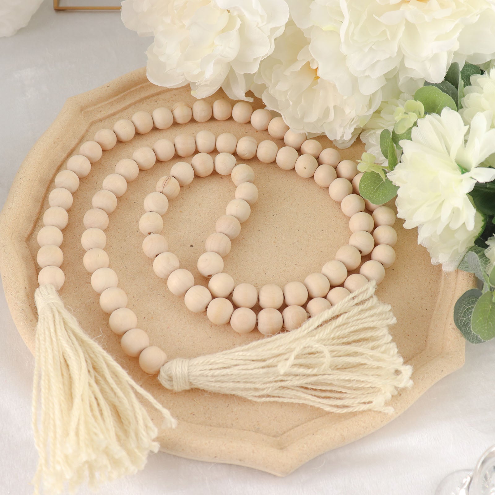 Cream rustic wood bead garland with tassels on a decorative tray.