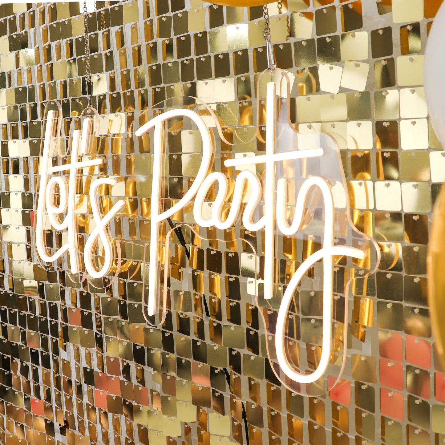 Ritzy gold sequin wall backdrop with neon "Let's Party" sign.