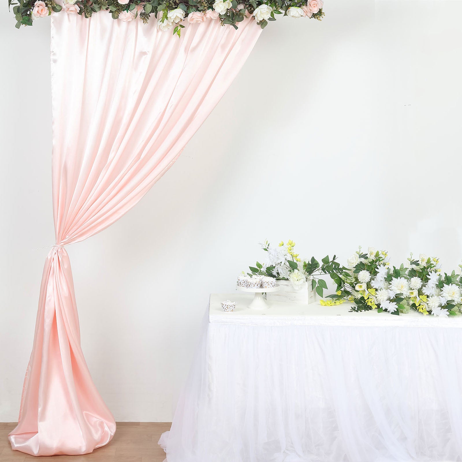 Blush satin event curtain drapes with floral backdrop and table setting.