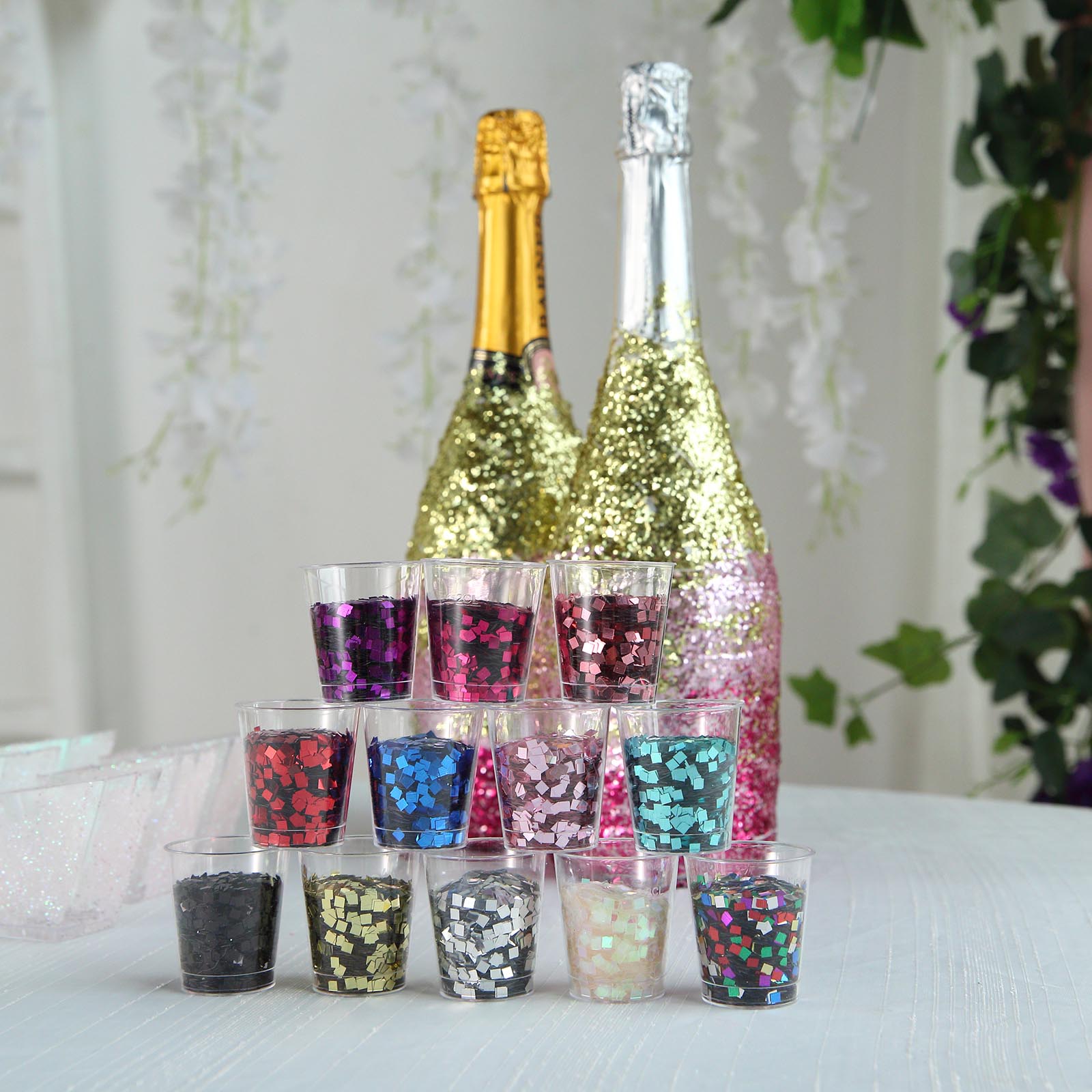 Metallic rose gold chunky confetti glitter in clear cups with champagne bottles.