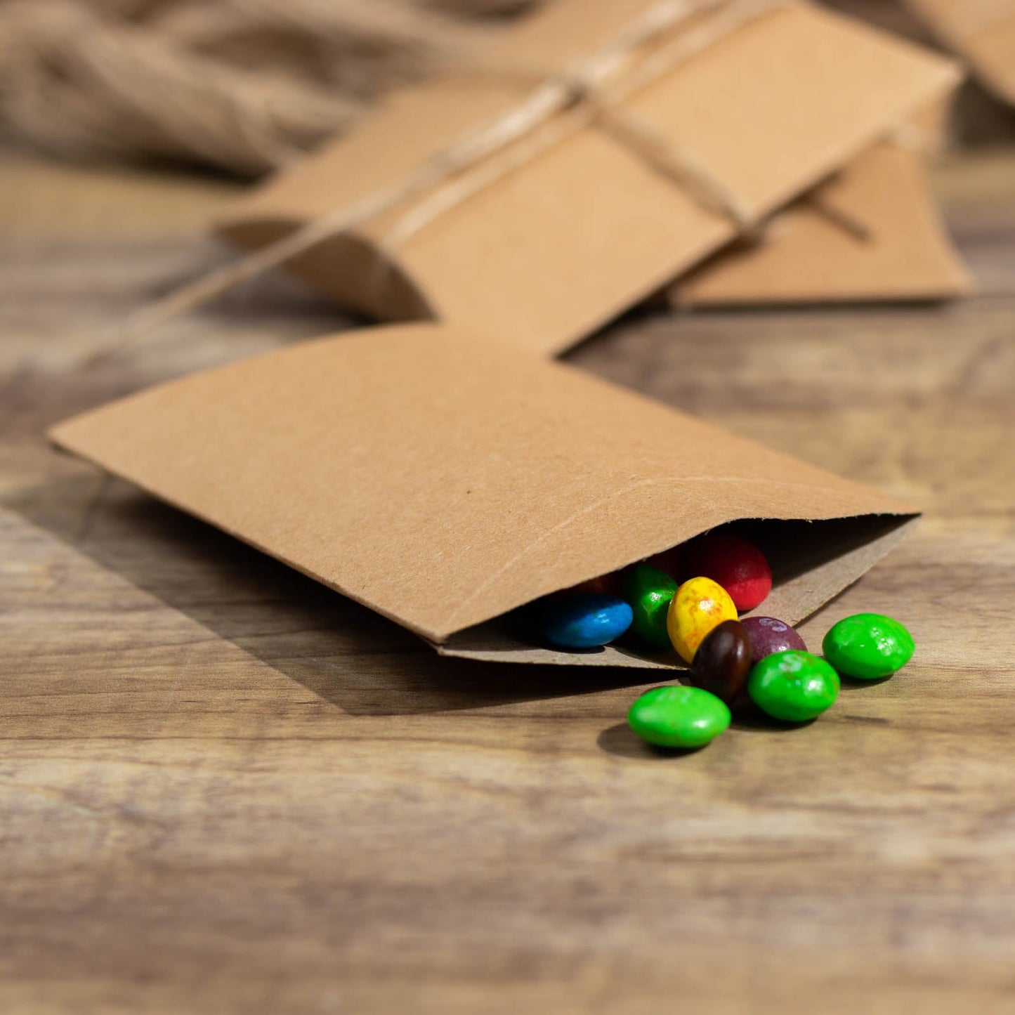 Natural brown paper wedding favor pillow boxes with colorful candies inside.