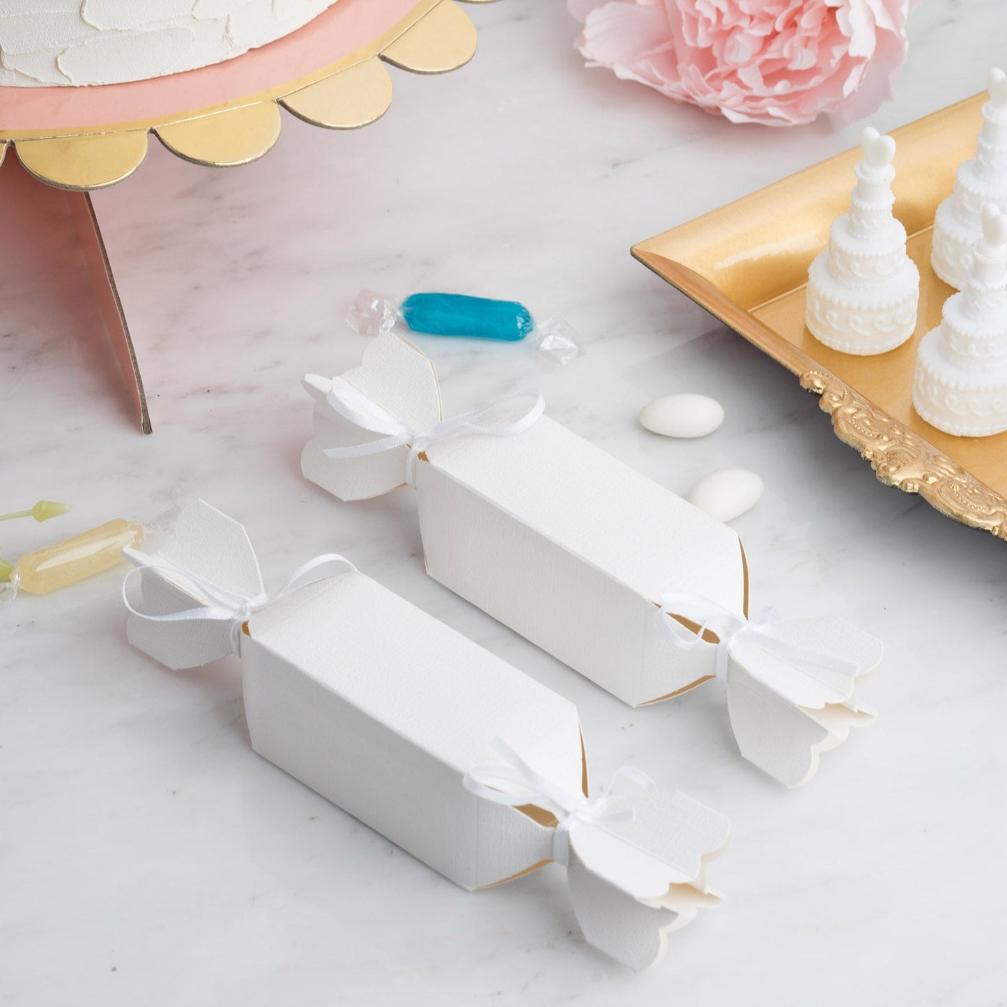White candy-shaped gift boxes with satin ribbon for party favors.