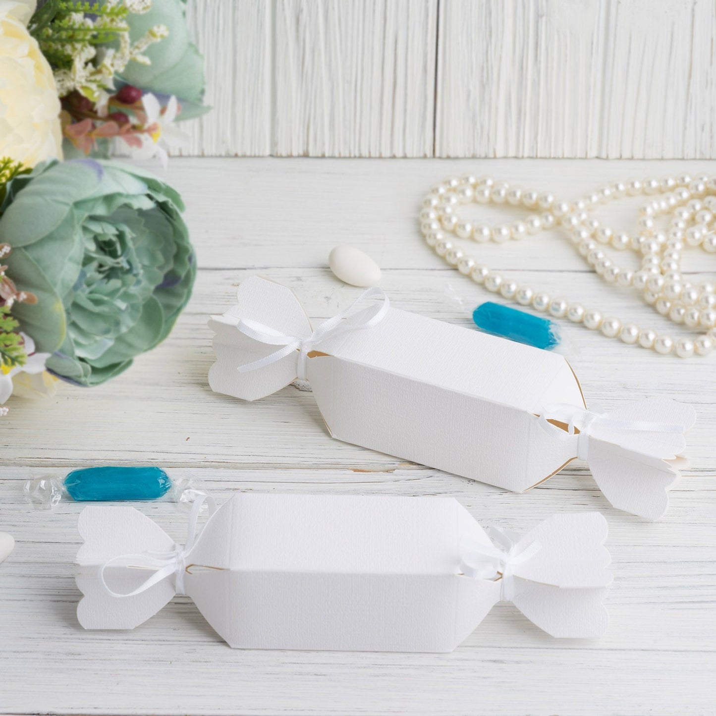 White candy-shaped party favor gift boxes with satin ribbons.