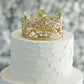 Matte gold metal princess crown cake topper on white wedding cake.