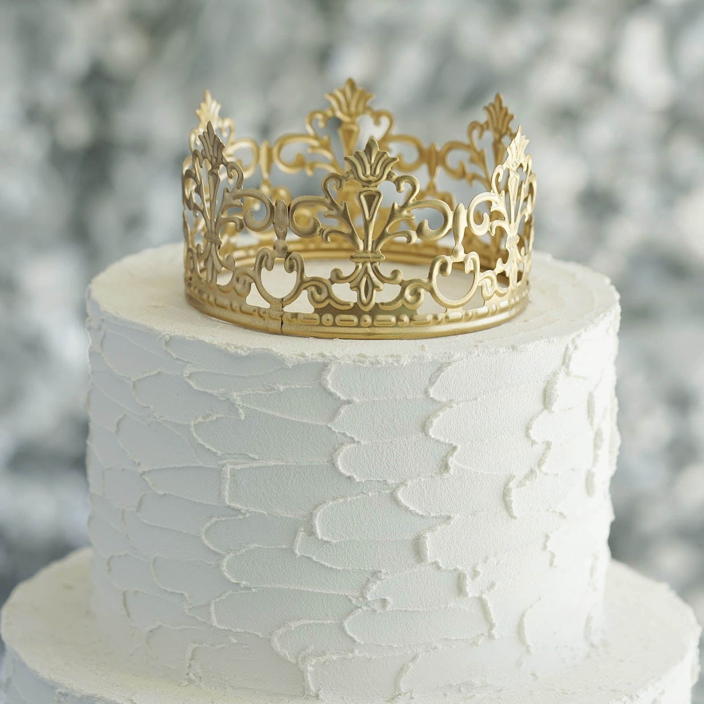 Matte gold metal princess crown cake topper on white wedding cake.