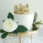 Matte gold metal princess crown cake topper on a wedding cake with floral decor.