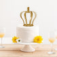 Matte gold metal royal crown cake topper on a white wedding cake.