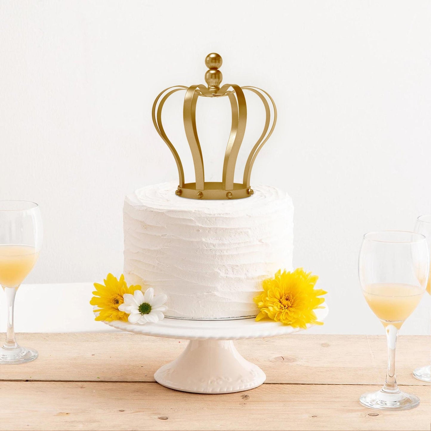 Matte gold metal royal crown cake topper on a white wedding cake.