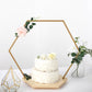 Gold hexagon floral hoop cake stand with wooden base and white cake.