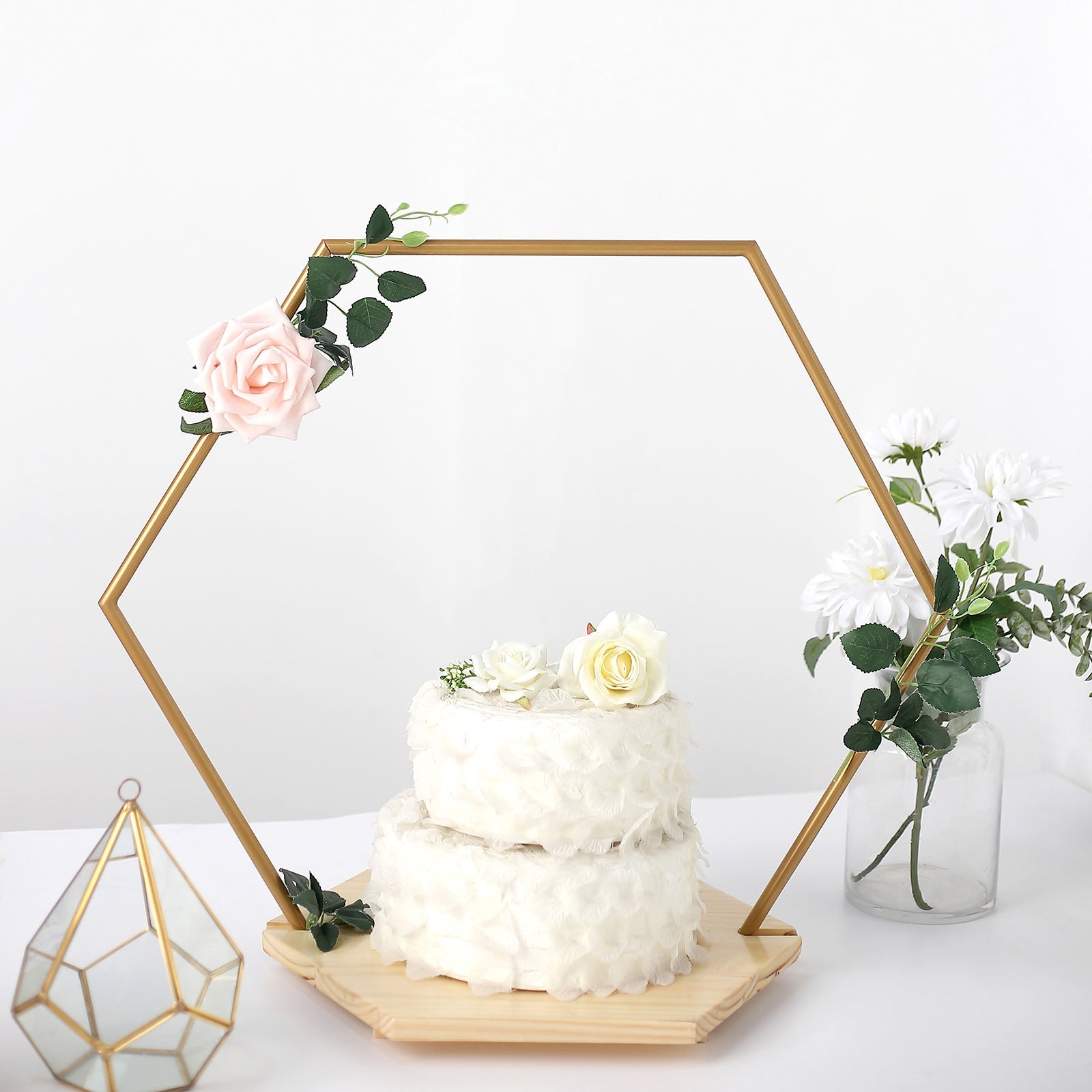 Gold hexagon floral hoop cake stand with wooden base and white cake.