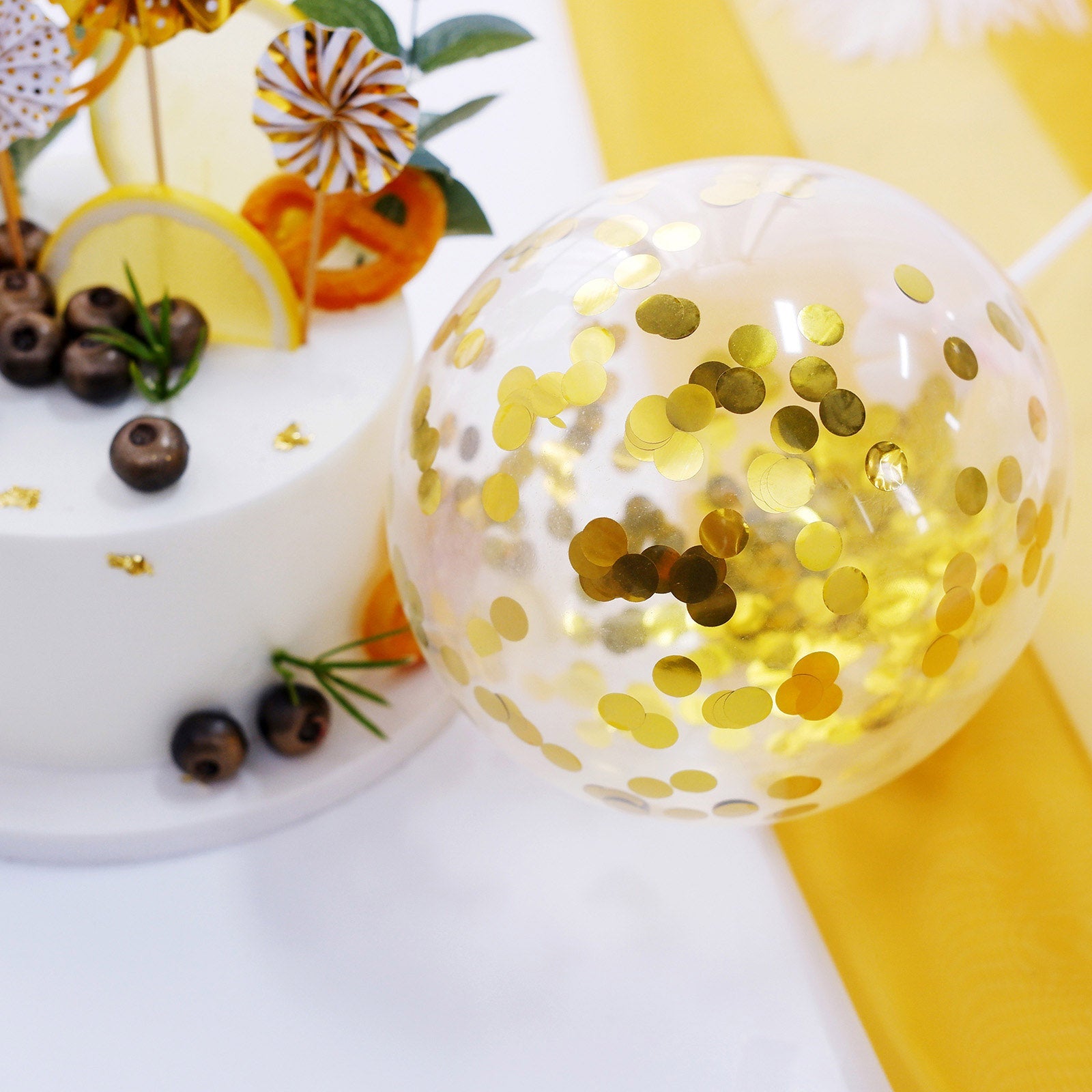Gold confetti balloon and cake topper with mini paper fans for birthday celebration.