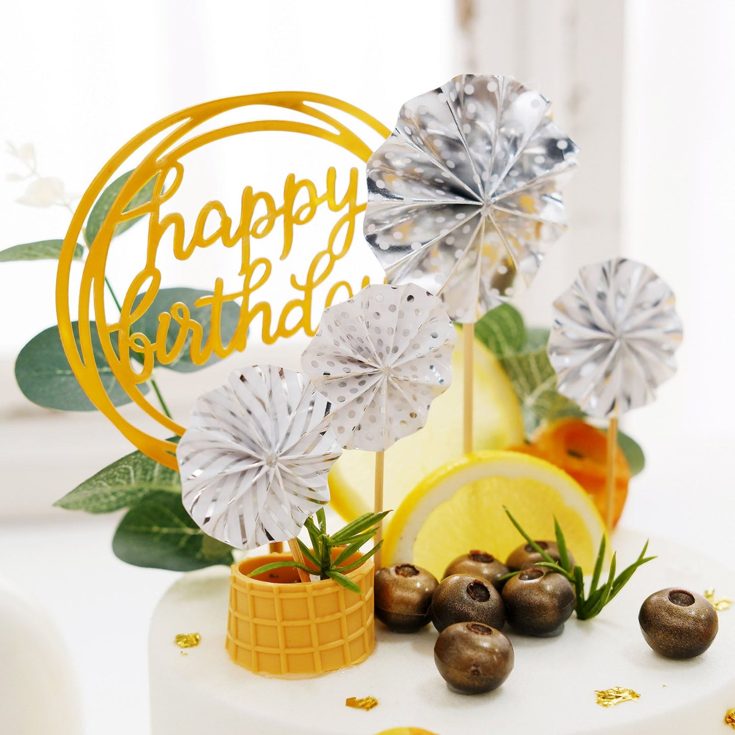 Silver and gold happy birthday cake topper with mini paper fans and balloon decor.