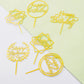 Gold acrylic happy birthday cake toppers in assorted styles.
