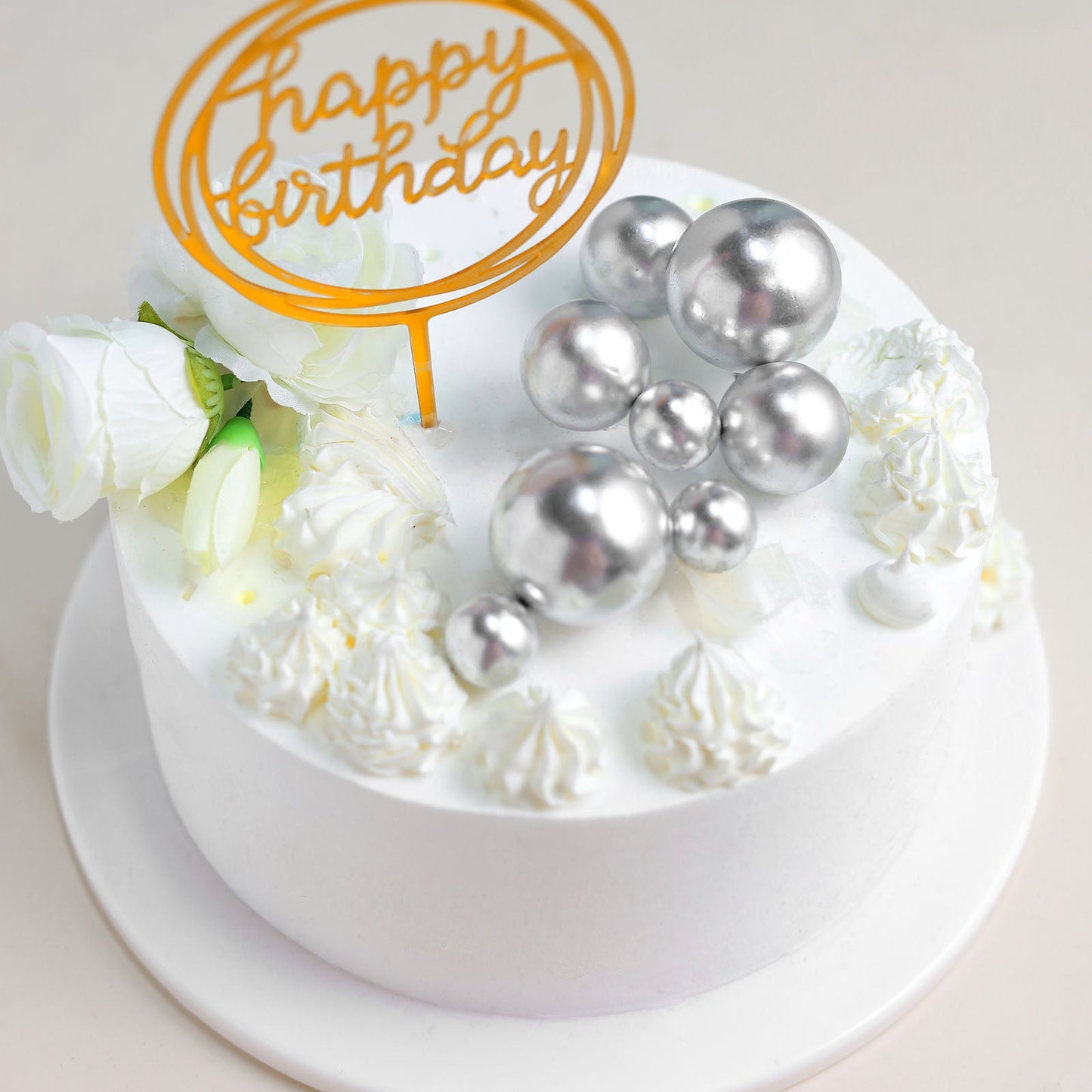 Silver faux pearl balls cake topper on a white birthday cake.