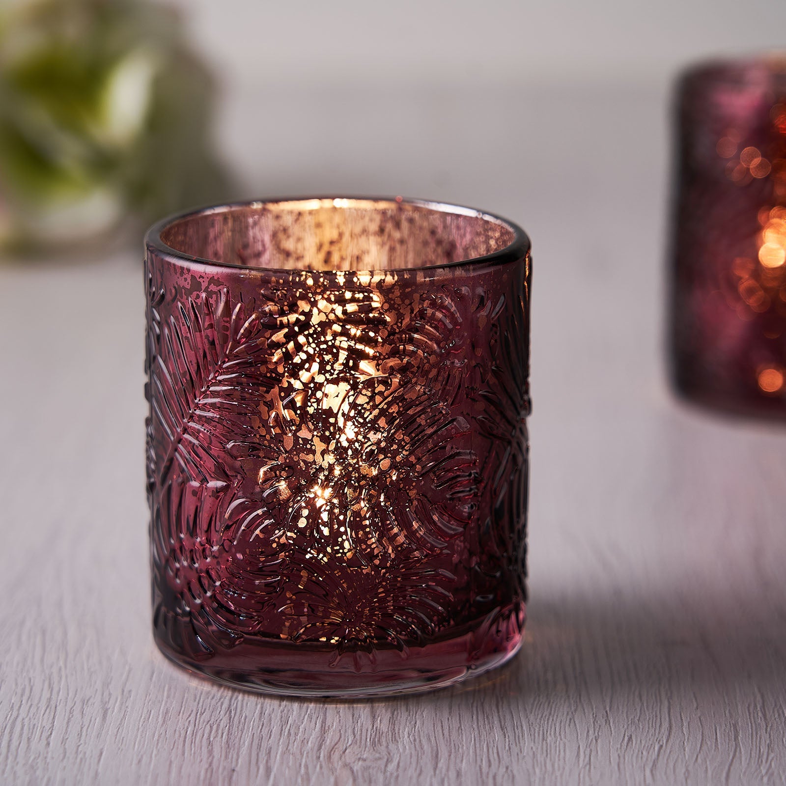 Burgundy glass palm leaf candle holder with warm glowing light.