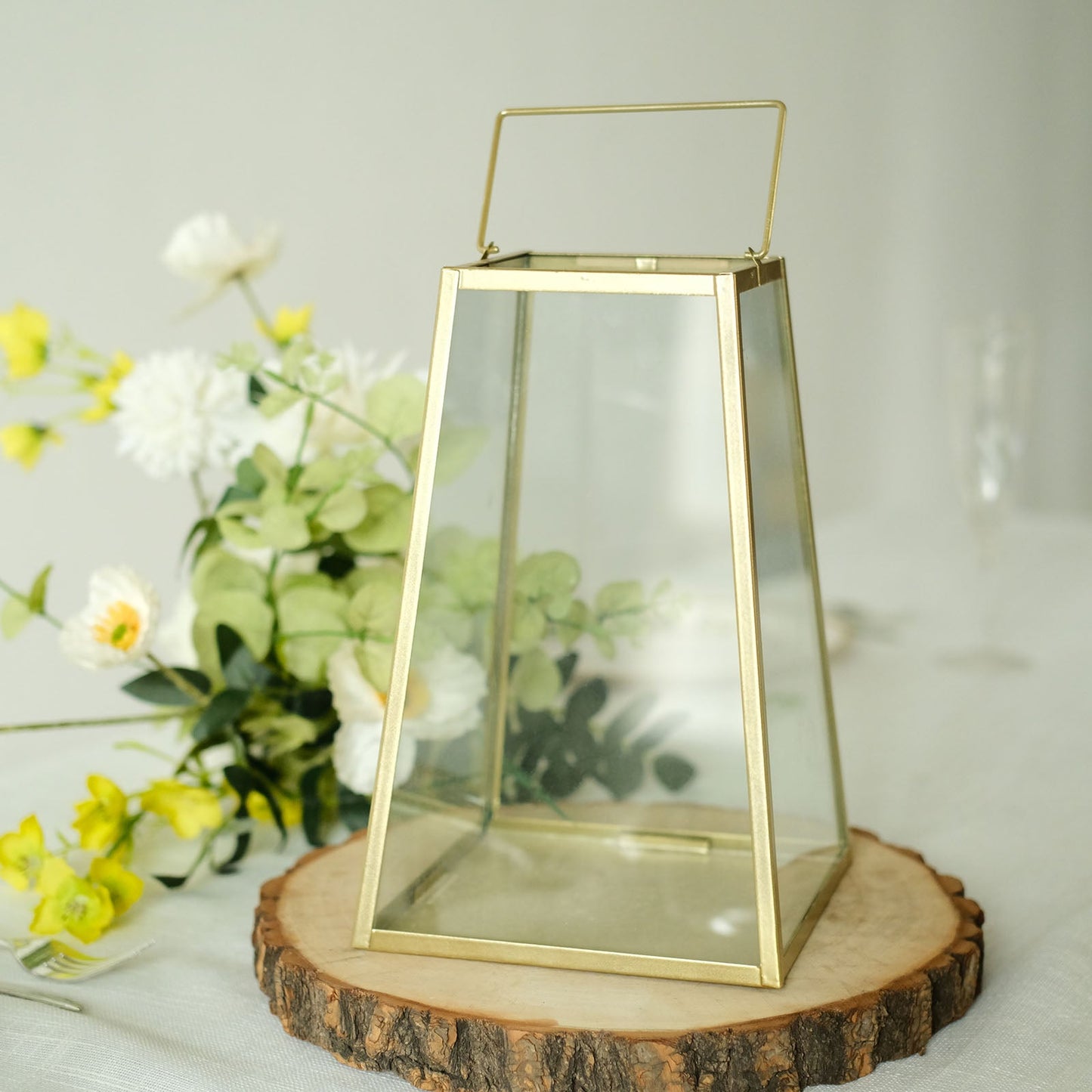 Gold trapezoid metal candle lantern with geometric design and clear glass.