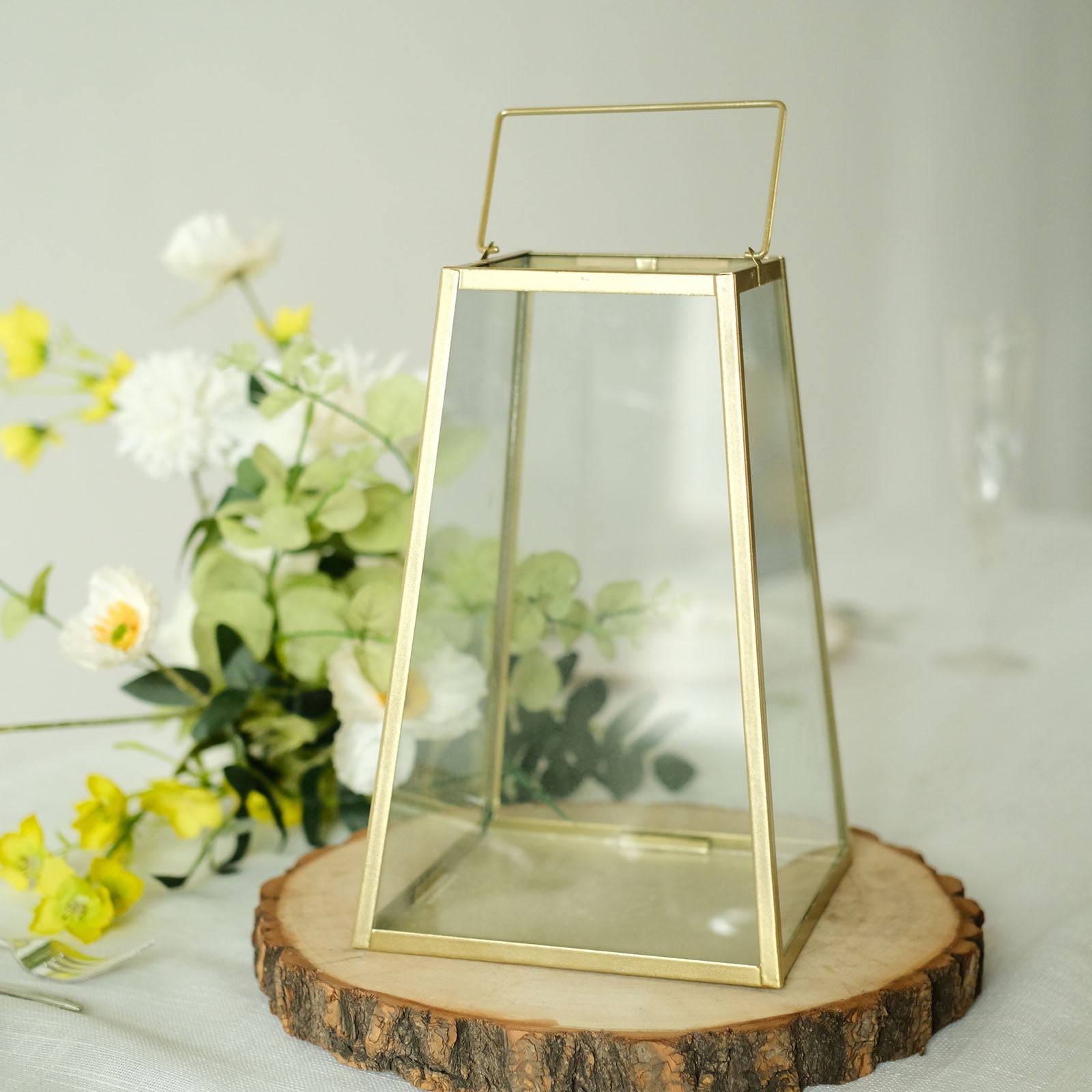 Gold trapezoid metal candle lantern with geometric design and clear glass.