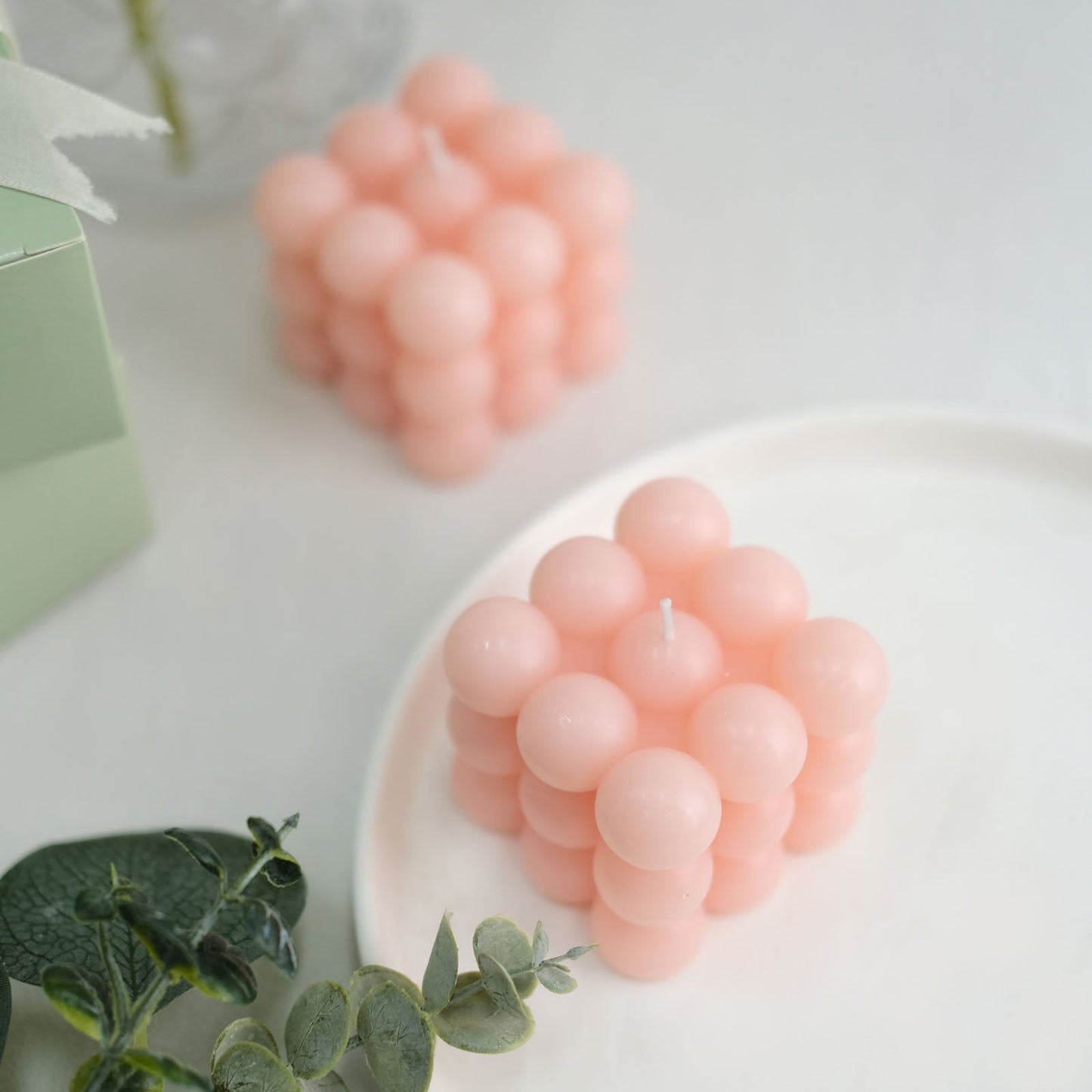 Pink decorative paraffin wax bubble candles on a white plate with greenery.