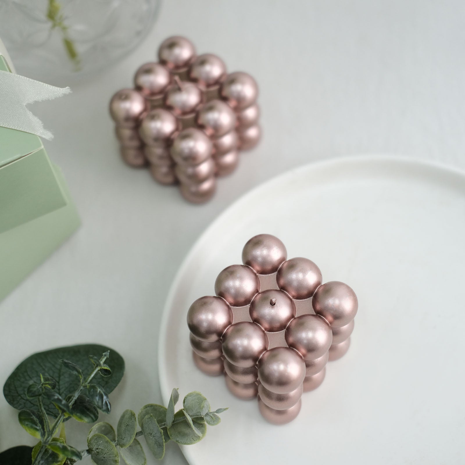Metallic rose gold bubble cube decorative candles set on a white plate.